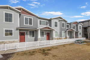 Townhome / multi-family property with a fenced front yard, stone siding, board and batten siding, and a residential view