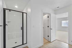 Full bathroom featuring visible vents, a stall shower, a textured ceiling, wood finished floors, and baseboards