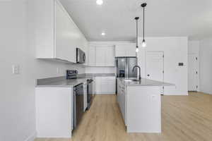 Kitchen featuring light wood finished floors, white cabinets, stainless steel appliances, and decorative light fixtures