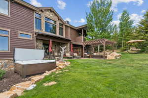 Rear view of house featuring a hot tub, stone siding, outdoor lounge area, and a pergola