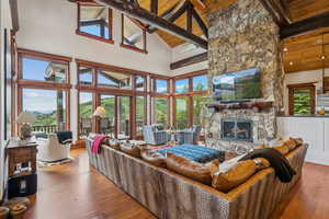 Living area with a stone fireplace, a wood ceiling with exposed beams, high vaulted ceiling, hardwood / wood-style flooring, and healthy amount of natural light
