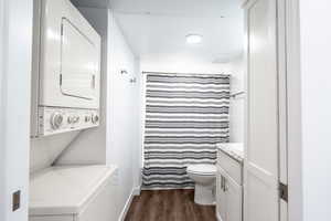 Bathroom featuring stacked washer / dryer, baseboards, toilet, wood finished floors, and vanity