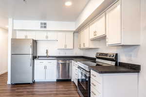 Kitchen featuring visible vents, dark wood-type flooring, a sink, dark countertops, and stainless steel appliances