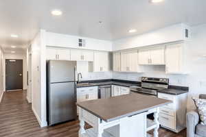 Kitchen featuring dark countertops, visible vents, dark wood finished floors, appliances with stainless steel finishes, and white cabinets