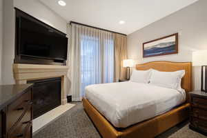 Bedroom featuring dark colored carpet, a fireplace with flush hearth, and recessed lighting