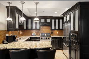 Kitchen with glass insert cabinets, high quality appliances, a peninsula, a raised ceiling, and a sink