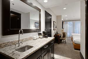 Kitchen featuring dark cabinetry, light stone countertops, recessed lighting, a sink, and light carpet