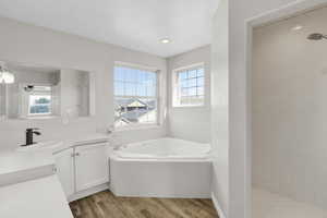 Full bath featuring a garden tub, a ceiling fan, wood finished floors, tiled shower, and vanity