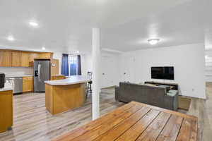 Kitchen featuring a breakfast bar, light countertops, light wood-style floors, appliances with stainless steel finishes, and open floor plan