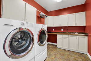 Clothes washing area with cabinet space, washer and dryer, baseboards, and a sink