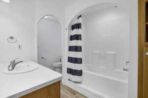 Bathroom with vanity, toilet, shower / bath combo with shower curtain, and wood finished floors