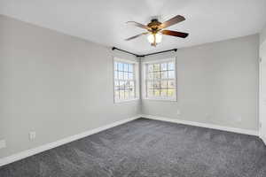 Empty room featuring a ceiling fan, baseboards, and dark colored carpet