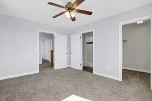 Unfurnished bedroom featuring carpet flooring, a ceiling fan, a walk in closet, and baseboards