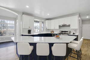 Kitchen with stainless steel gas range oven, under cabinet range hood, a sink, white cabinetry, and light countertops