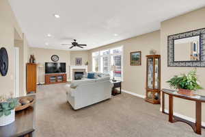 Carpeted living room featuring a glass covered fireplace, recessed lighting, a ceiling fan, and baseboards