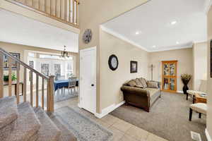 Carpeted living area featuring crown molding, baseboards, stairs, recessed lighting, and tile patterned floors