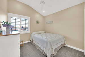 Carpeted bedroom with vaulted ceiling, a ceiling fan, and baseboards