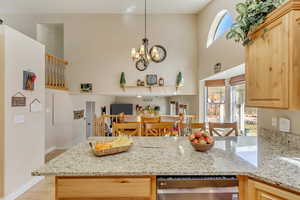 Kitchen featuring light brown cabinetry, a chandelier, a towering ceiling, and light stone countertops