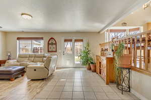Living area with light tile patterned floors, visible vents, a textured ceiling, and baseboards