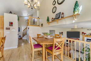 Dining area featuring baseboards, stairs, a fireplace, light wood-style floors, and high vaulted ceiling