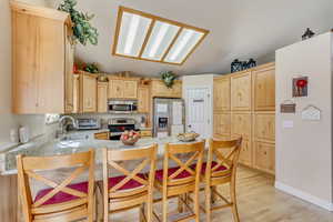 Kitchen featuring light brown cabinetry, a peninsula, stainless steel appliances, and a kitchen breakfast bar