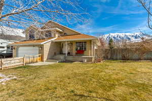 View of front of home with fence, a porch, brick siding, a front lawn, and a mountain view