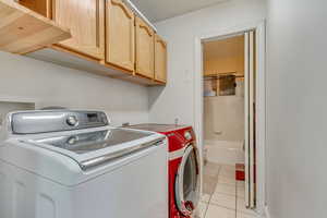 Washroom featuring light tile patterned flooring, cabinet space, and washing machine and clothes dryer