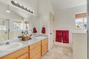 Full bathroom with double vanity, vaulted ceiling, a stall shower, and a sink