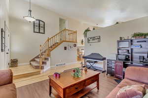 Living room featuring stairs, a high ceiling, light wood-style flooring, and visible vents