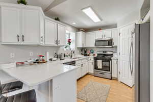 Kitchen featuring light wood-style flooring, a peninsula, stainless steel appliances, white cabinetry, and a sink