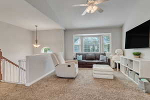 Carpeted living area with vaulted ceiling, a ceiling fan, and baseboards