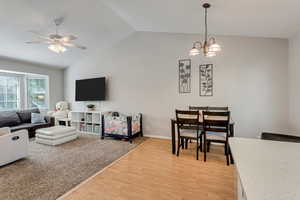 Living room featuring baseboards, ceiling fan with notable chandelier, light wood-style flooring, and vaulted ceiling