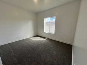 Spare room with dark colored carpet, visible vents, and baseboards