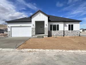 View of front of house with stone siding, board and batten siding, concrete driveway, and a garage