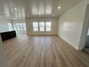 Unfurnished living room featuring recessed lighting, baseboards, light wood-style floors, and a textured ceiling