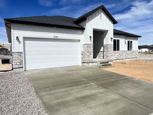 View of front facade featuring stone siding, concrete driveway, an attached garage, and a shingled roof