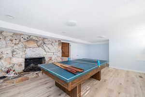 Recreation room featuring a fireplace, a textured ceiling, baseboards, and wood finished floors