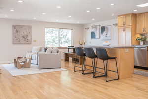 Kitchen featuring a kitchen island, recessed lighting, dishwasher, light wood-type flooring, and a kitchen bar