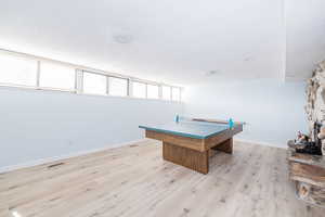 Rec room with visible vents, baseboards, a stone fireplace, and light wood-style floors