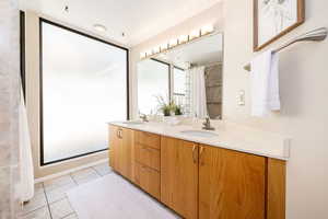 Bathroom featuring tile patterned flooring, curtained shower, double vanity, and a sink