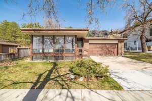 Mid-century inspired home featuring a front lawn, fence, concrete driveway, a garage, and brick siding