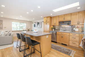 Kitchen featuring a breakfast bar, light wood-style flooring, a sink, open shelves, and dishwasher