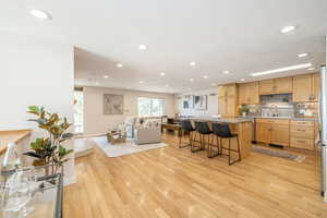 Kitchen featuring light wood-style flooring, a sink, dishwasher, open floor plan, and a kitchen bar