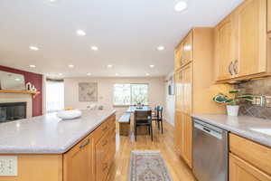 Kitchen featuring light wood-style flooring, a tiled fireplace, a kitchen island, tasteful backsplash, and dishwasher