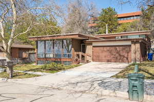 Mid-century inspired home featuring brick siding, fence, concrete driveway, a garage, and a sunroom