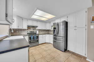 Kitchen featuring a sink, stainless steel appliances, white cabinets, under cabinet range hood, and tasteful backsplash