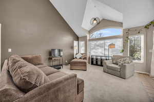 Living room featuring light tile patterned floors, light colored carpet, baseboards, and high vaulted ceiling