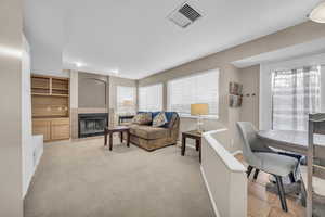 Living room featuring a tiled fireplace, baseboards, visible vents, and light carpet