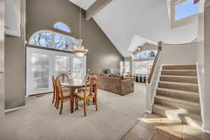 Carpeted dining area featuring beam ceiling, stairway, baseboards, and high vaulted ceiling