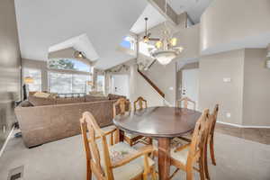 Dining room with visible vents, light carpet, a notable chandelier, and high vaulted ceiling